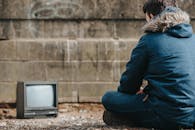 Crop man sitting against vintage TV on street