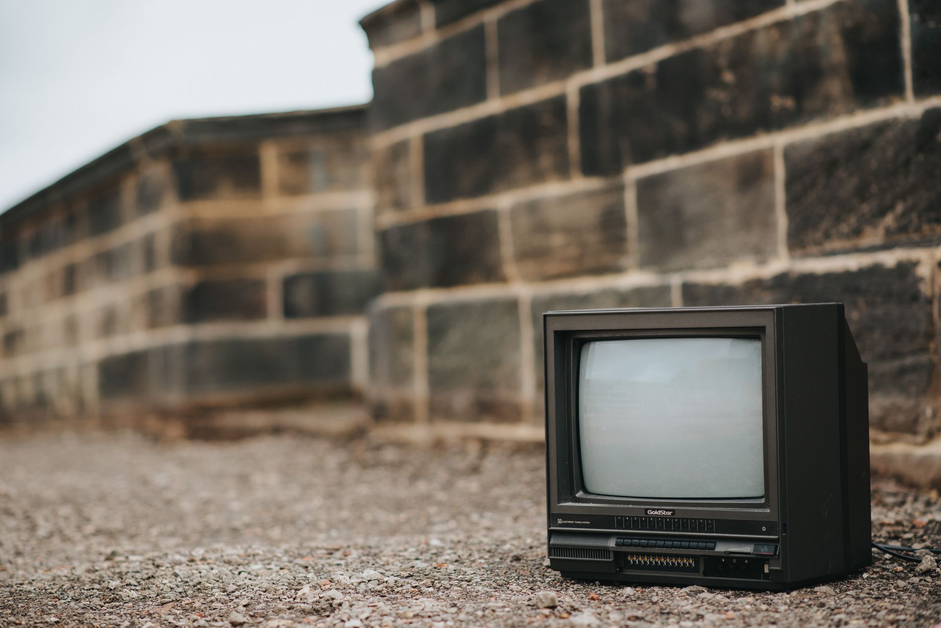 Small retro TV on ground near stone barrier