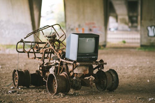 Small black old fashioned television placed on rusty metal construction under stone bridge with graffiti on blurred background in street