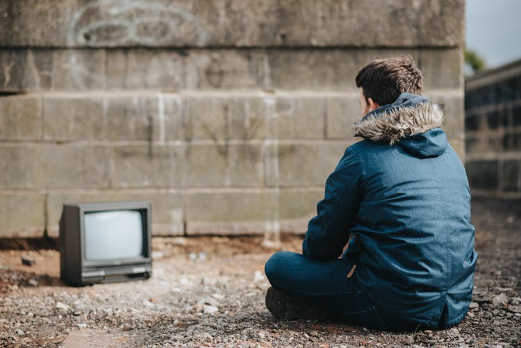 Anonymous Man Sitting Against Retro TV Set On Street