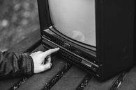 Black and white of unrecognizable male pressing buttons on old fashioned television placed on wooden table in nature on blurred background