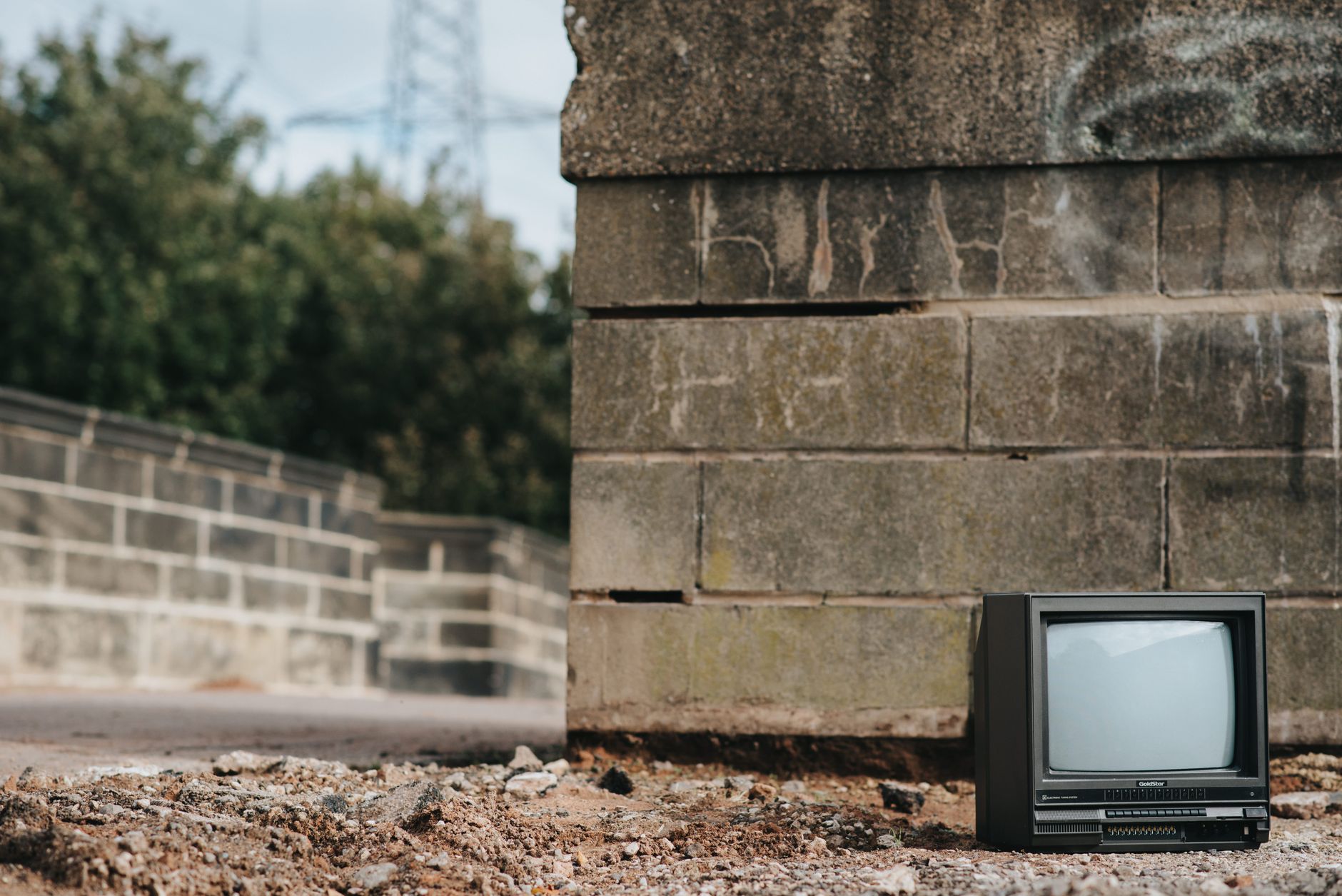 Small black old fashioned television placed on ground near concrete barrier with graffiti in city on street with trees on blurred background