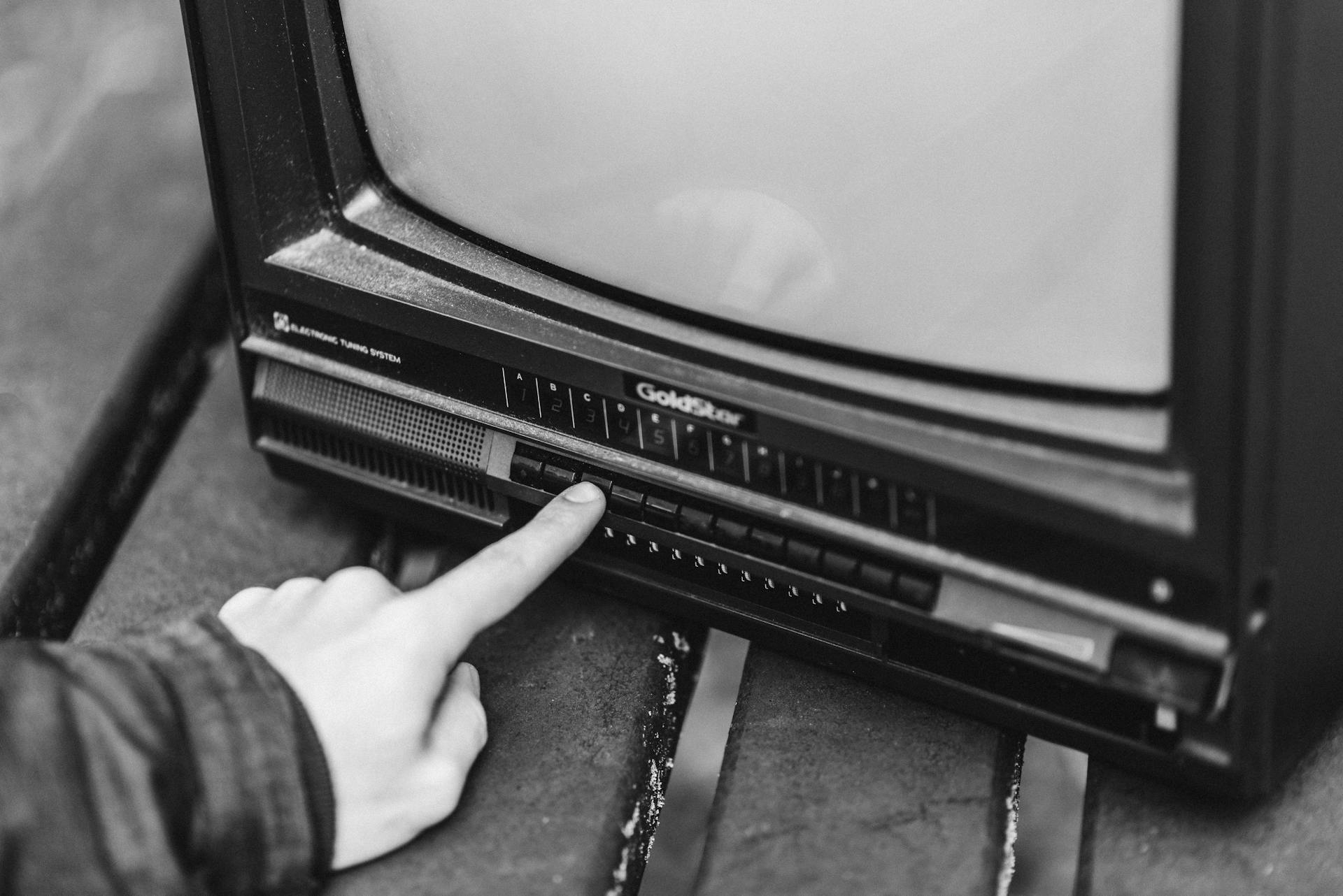 Black and white from above of anonymous male switching channels on retro black television placed in wooden table on street