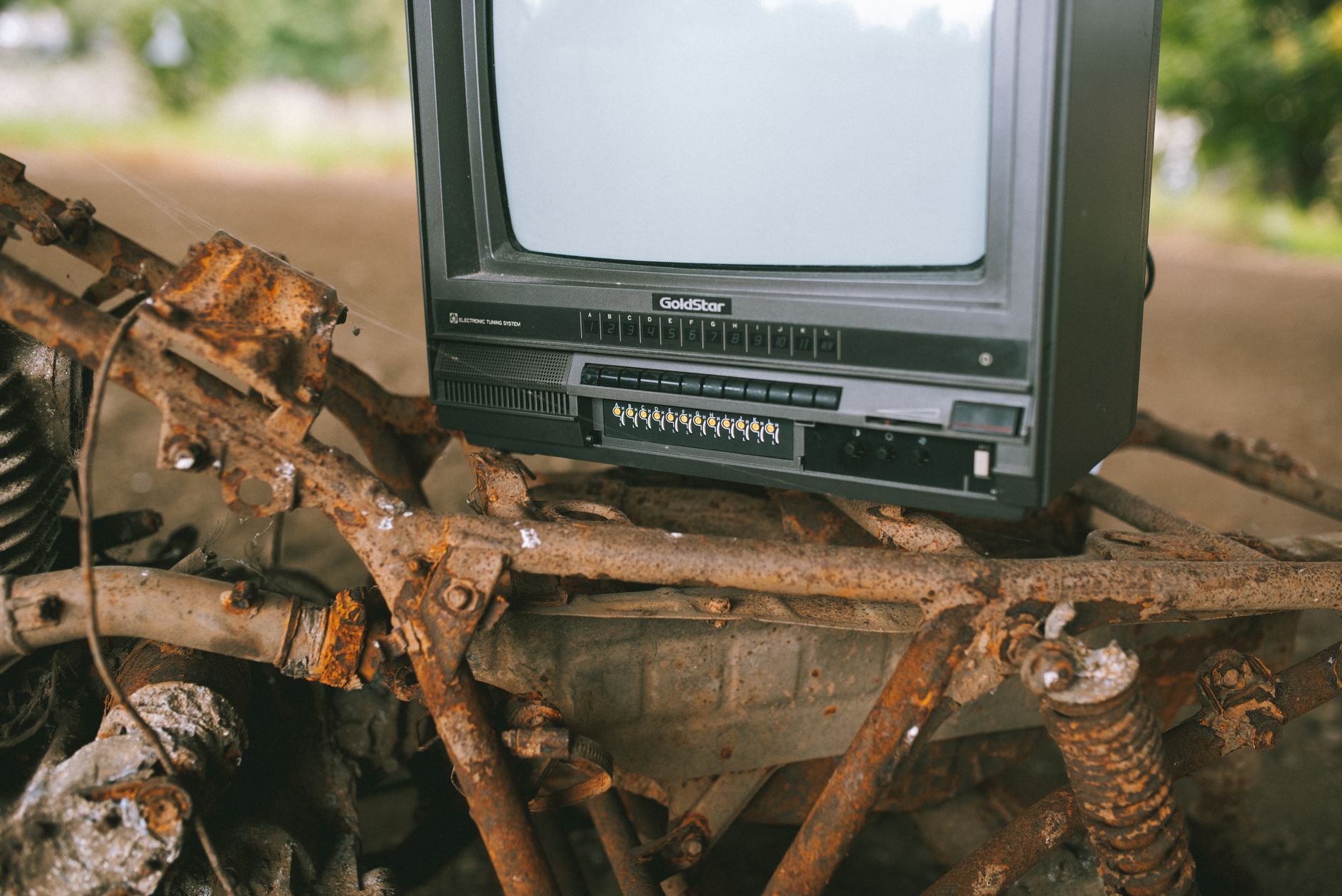Small black old fashioned obsolete television placed on rusty metal construction on street in city with trees on blurred background