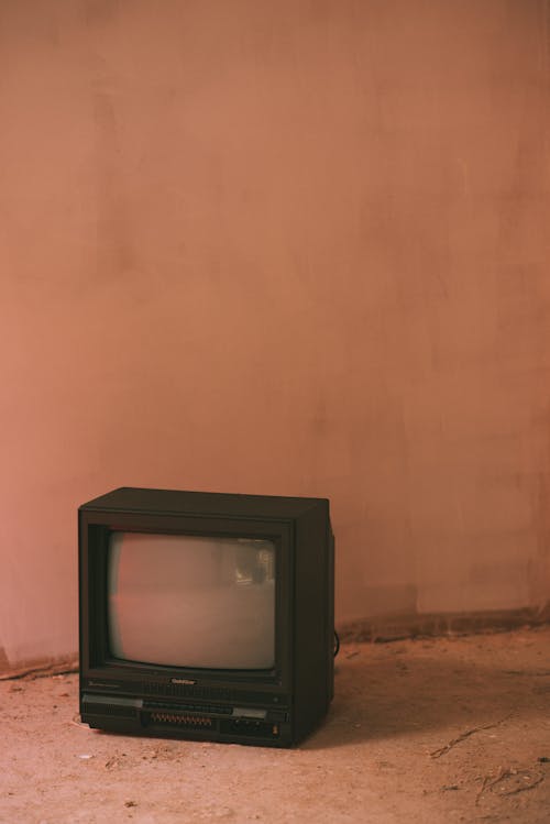 Small old fashioned television set on cement floor near wall in building in daytime