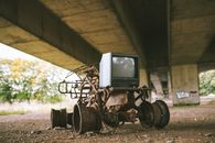 Old damaged vehicle with vintage television set on rough pathway under bridge in sunlight