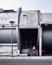 Man in Red Jacket and Black Pants Sitting on Gray Concrete Wall