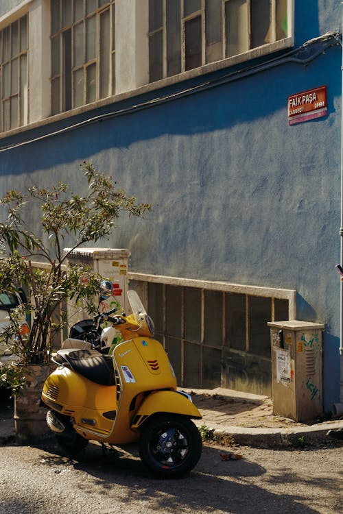 Free Yellow Motor Scooter Parked Beside Blue Painted Wall Stock Photo