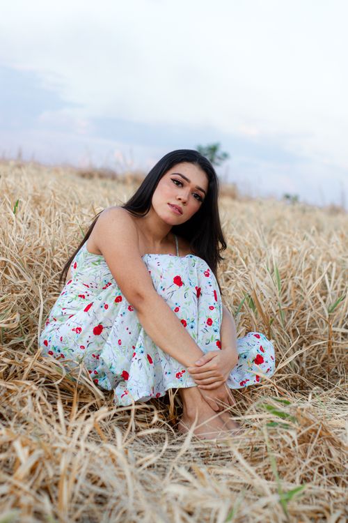 Free Young woman in floral dress sitting in a dry grass field during daytime. Stock Photo