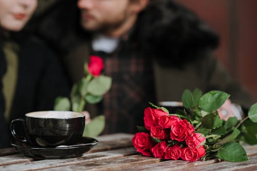 茶色の木製テーブルの上の黒いセラミックボウルの横にある赤いバラ