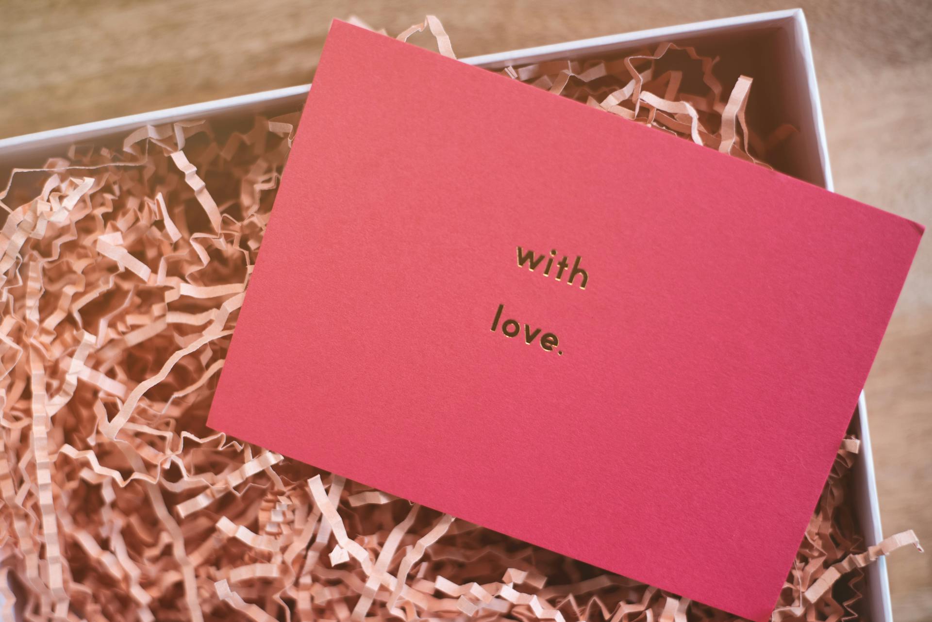 From above of rectangular shaped greeting card representing With Love inscription on cardboard box with organic shavings