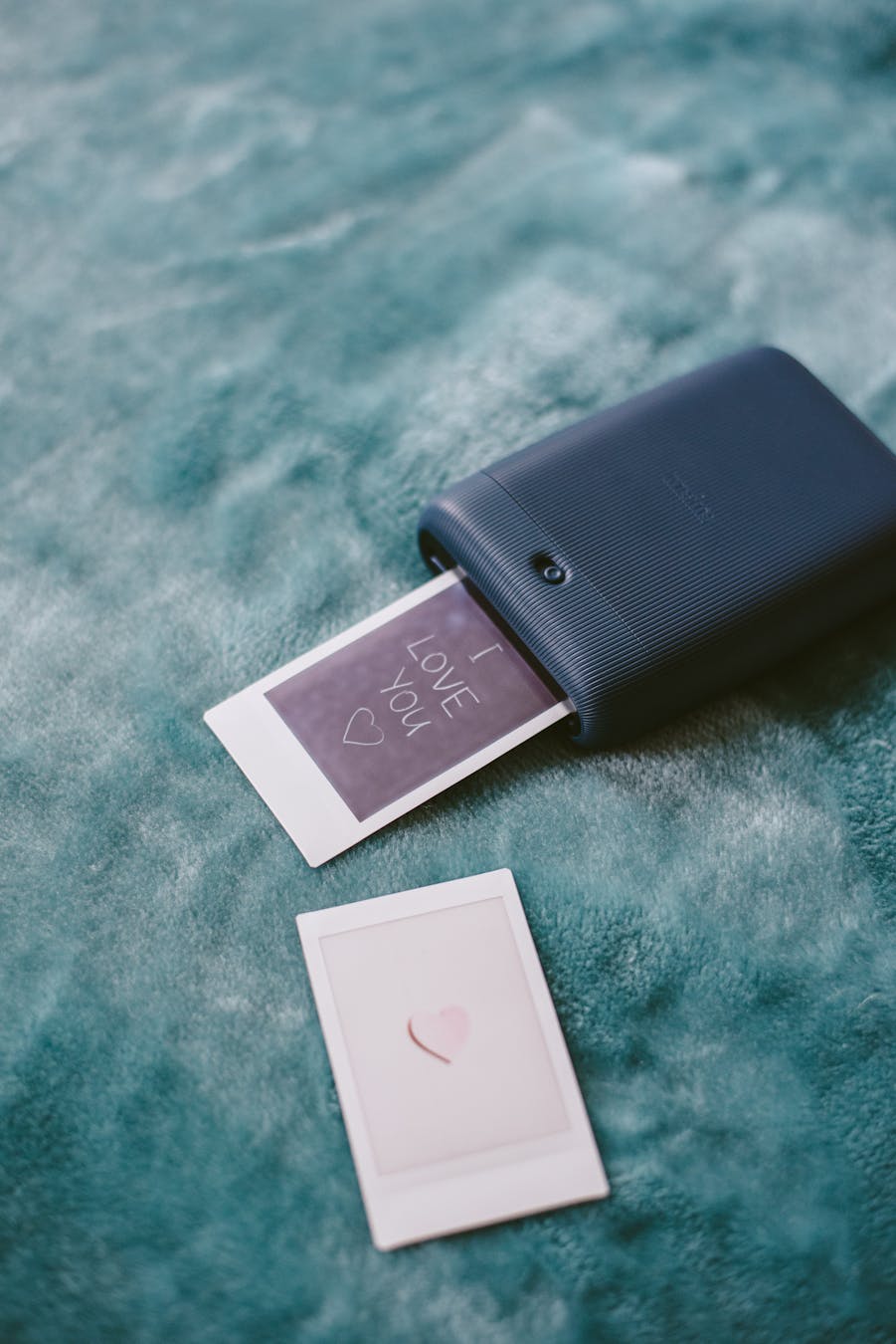 High angle of modern instant camera printing photo with heart symbol on plaid in daylight