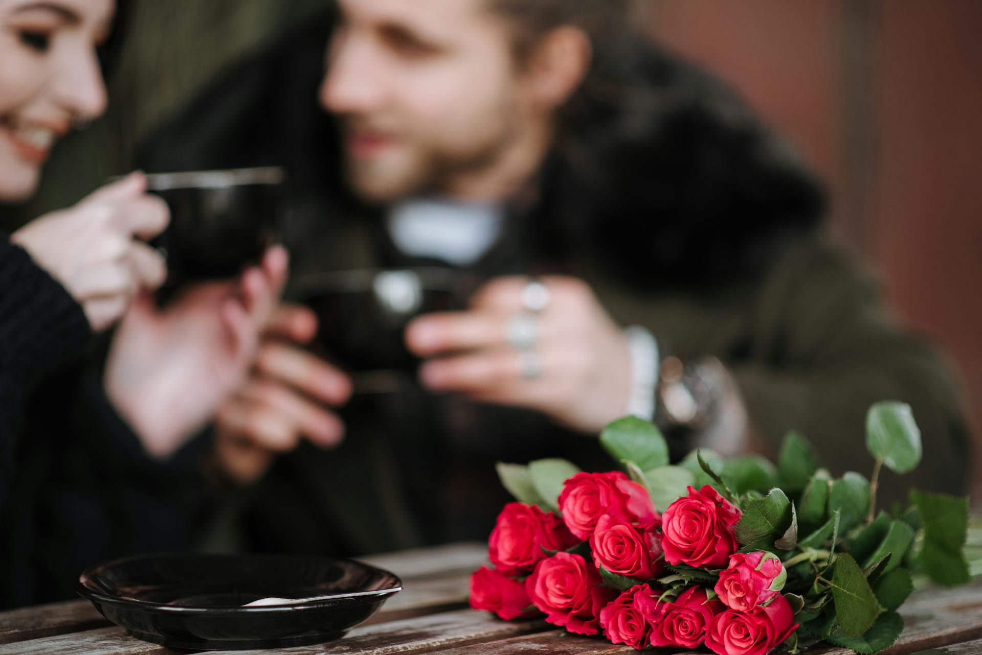 Crop couple with coffee interacting at cafe table with flowers