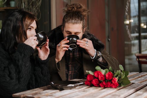 Couple enjoying delicious coffee at cafe table with blossoming roses