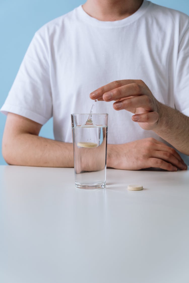 A Person Dropping An Effervescent Tablet Into A Glass Of Water