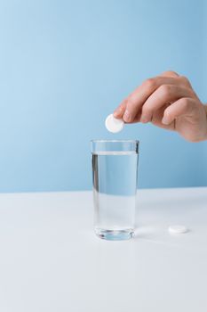 一只手将一块滑石粉放入浅蓝色背景的水杯中