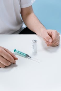 Close-up of hands with a syringe and vial on a white surface, representing medical care.