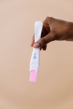 这是一张特写图像，背景为米色，画面中一只手拿着阳性妊娠测试