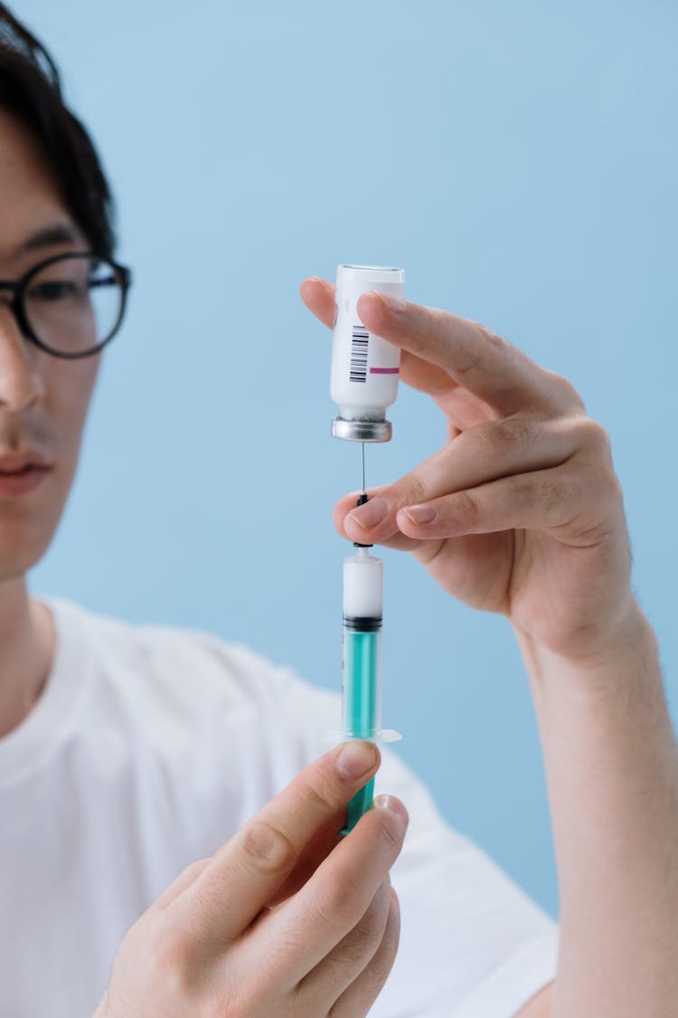 A Man Filling A Syringe With Fluid From A Vial