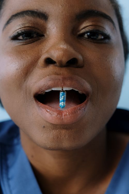 Free African American woman holds a colorful capsule in her mouth, capturing focus on medication. Stock Photo