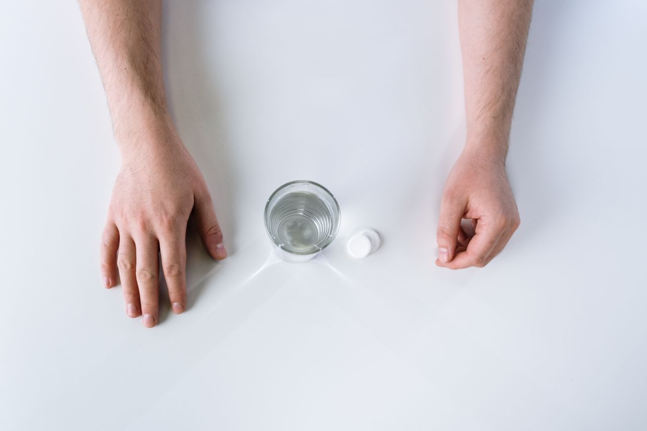 Top view of two hands beside a glass of water and two white tablets