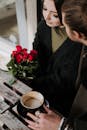 From above of crop anonymous man with cup of cappuccino talking to charming female beloved with flowers in cafeteria