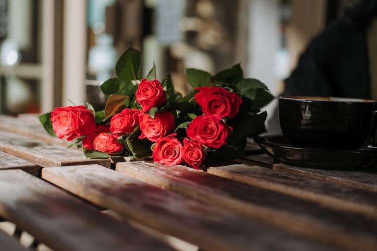 Bright Blooming Roses Near Cup Of Coffee In Cafe