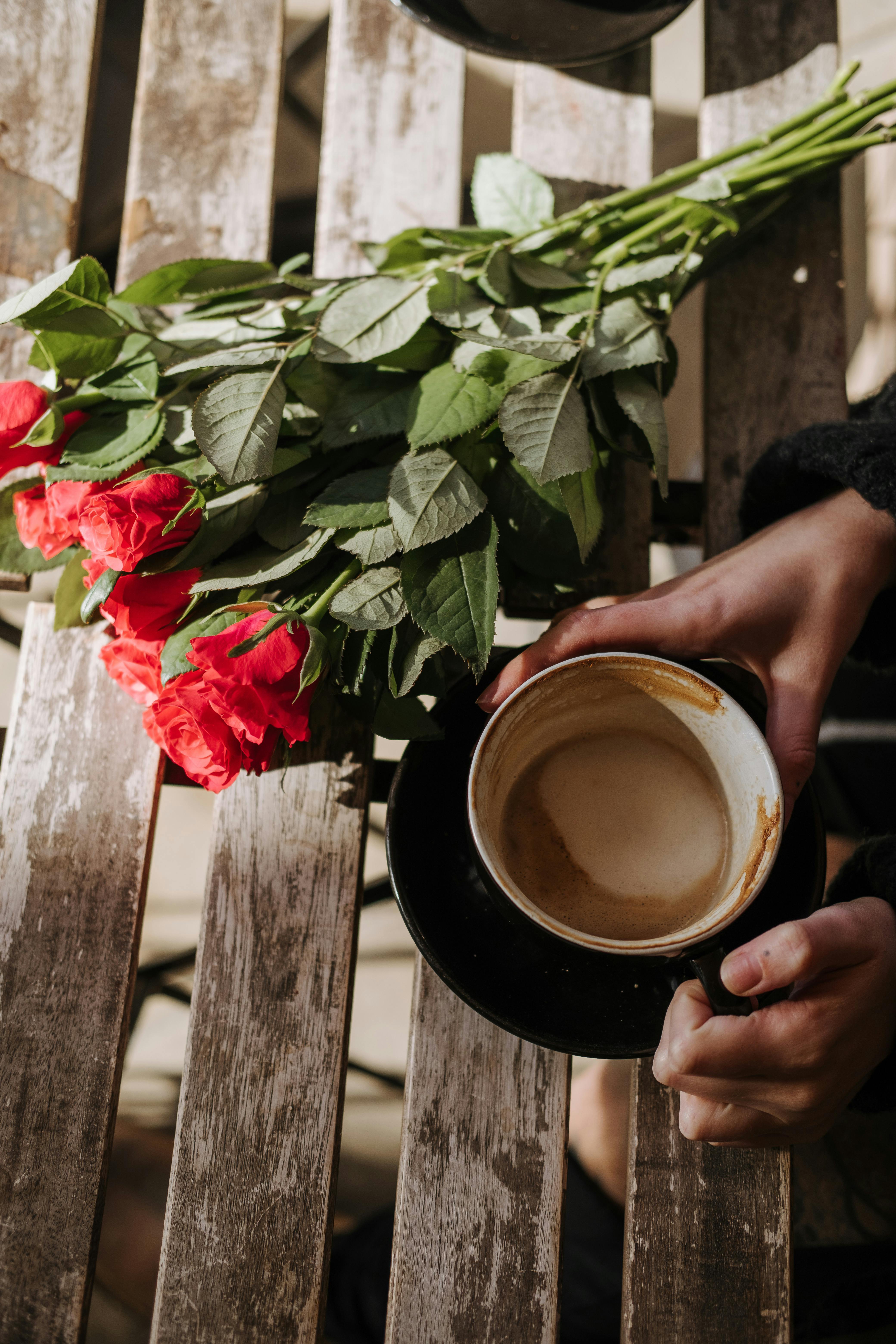 crop person with cup of cappuccino and roses in cafe
