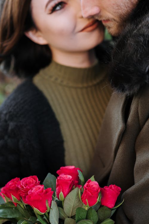 赤いバラを保持している茶色のコートの女性