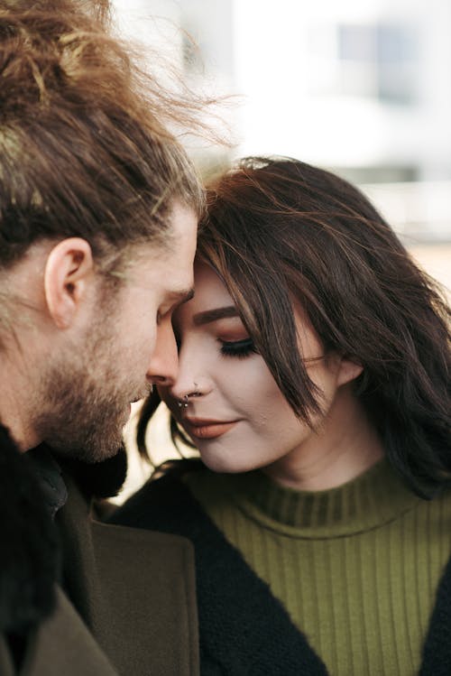 Loving young couple in stylish outfits touching foreheads with closed eyes on city street in daytime