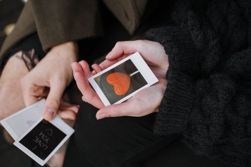 Free From above of anonymous couple in warm outerwear sitting with photos of heart shaped candy and romantic inscription during date Stock Photo