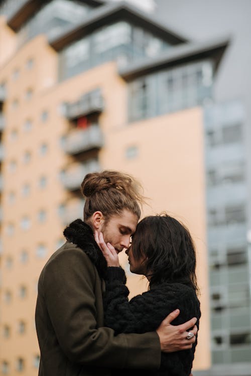Free Side view of romantic couple embracing each other while standing on street against residential house on blurred background in city Stock Photo