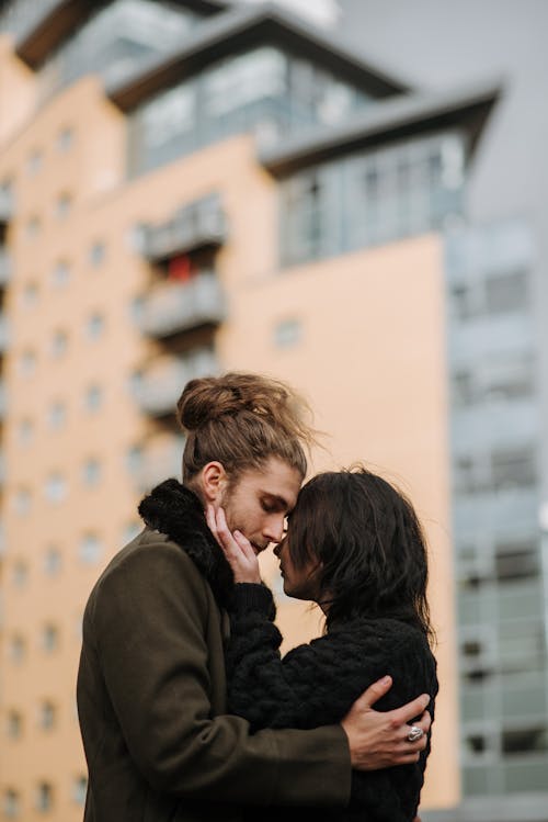 Side view of romantic couple embracing each other while standing on street against residential house on blurred background in city