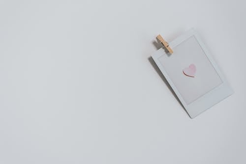 Free Top view of photo with small pink heart with wooden photo paper peg pin placed on white background during holiday celebration Stock Photo