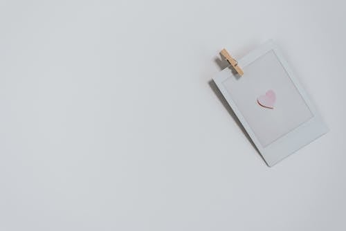 Top view of photo with small pink heart with wooden photo paper peg pin placed on white background during holiday celebration