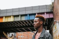 Side view of African American male standing in city on street with rainbow LGBT paint on structure against blurred background