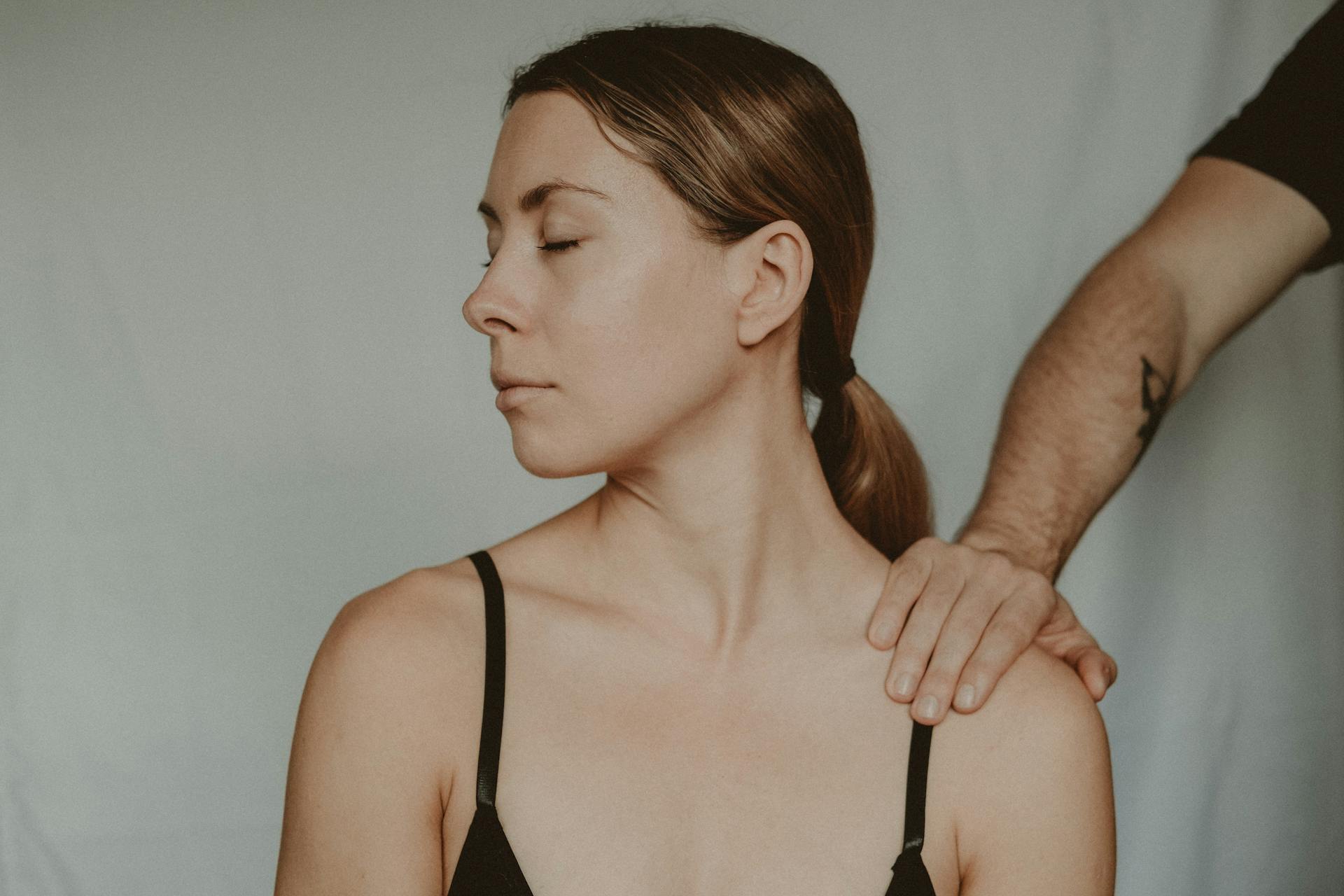 Calm and serene massage therapy session showing a woman receiving a shoulder massage, eyes closed.