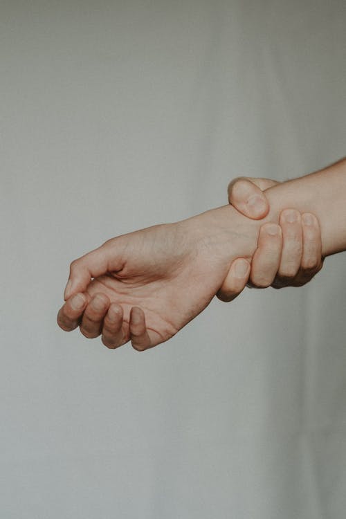 Free Unrecognizable person holding tight wrist of anonymous person trying to stop on grey background Stock Photo