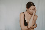 Young slender female in black bra standing with closed eyes covering face with hand