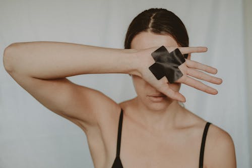 Faceless young lady in black underwear showing hand with black cross tape against abuse on white background