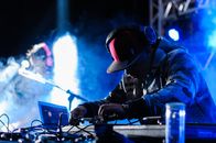 Side view of concentrated African American DJ in headphones performing music at concert in club with neon lights