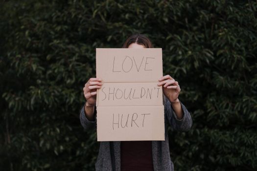 Faceless woman demonstrating in hands poster against abuse