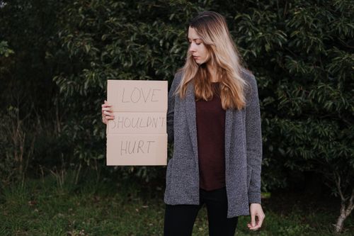 Free Lady in casual clothes standing near green bushes while showing poster saying Love Should Not Hurt Stock Photo