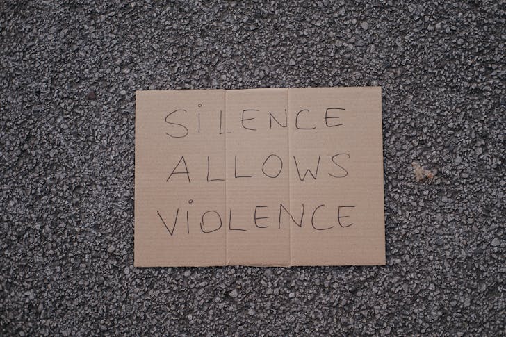 Top view of slogan silence allows violence on carton placed on rough asphalt road on street