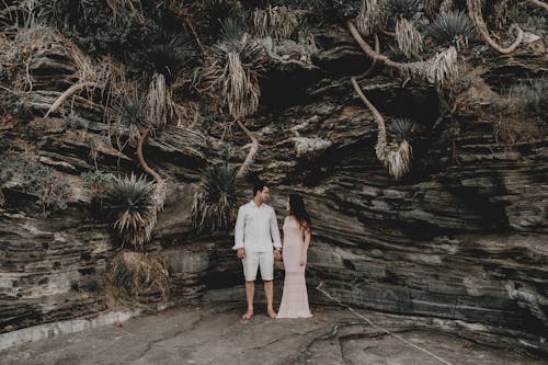 Full body of young couple in elegant clothes standing close to each other in rocky cave