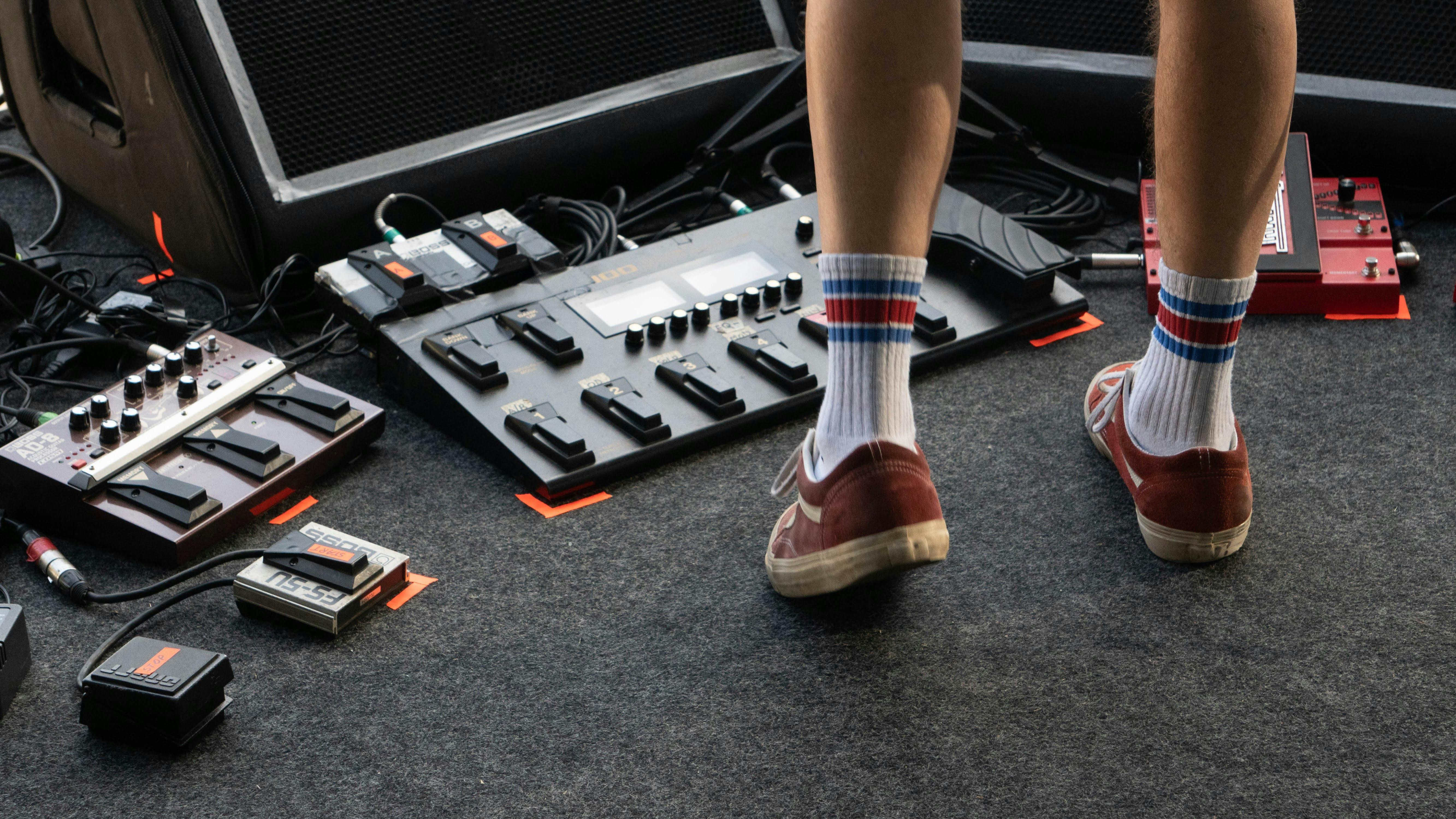 crop man on stage with pedalboard