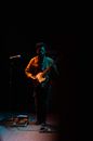 Full body of talented musician playing electric guitar on stage near microphone stand while performing song during live concert in darkness
