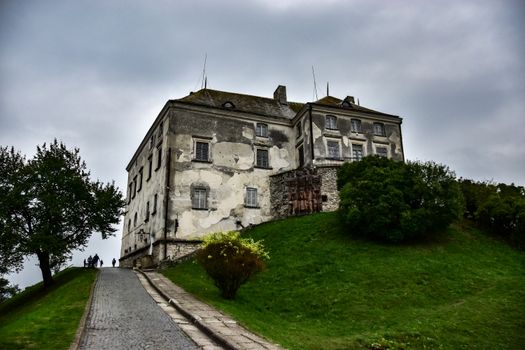 A weathered historical building sits dramatically on a lush green hill under a cloudy sky.