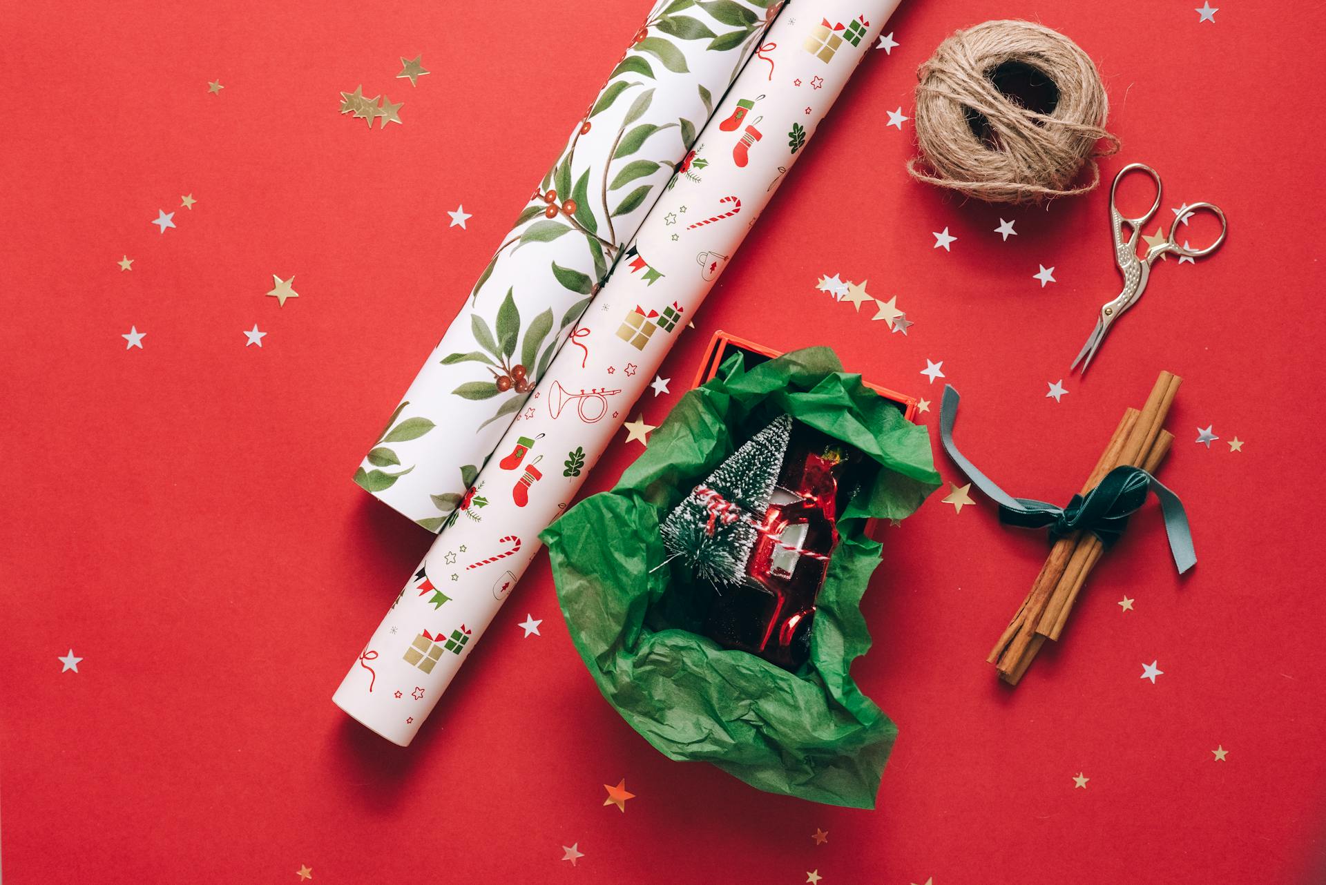 Christmas gift wrapping essentials on a red background with decorative elements and a toy car.