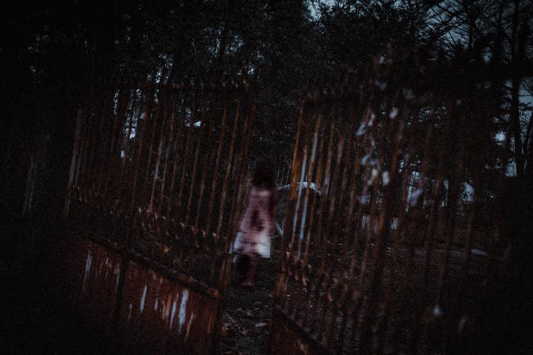 Unrecognizable Zombie Woman Walking In Park Near Aged Metal Fence